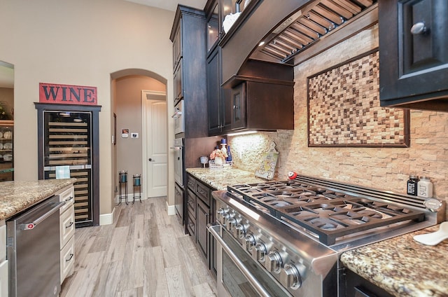 33215 Worthing Ln, Fulshear, TX 77441 - kitchen featuring appliances with stainless steel finishes, arched walkways, wine cooler, decorative backsplash, and light wood-type flooring