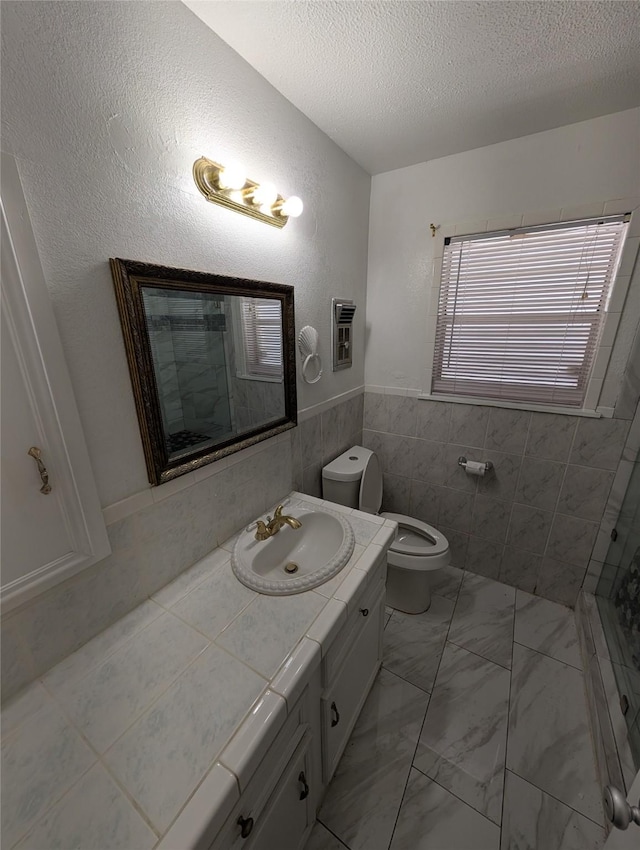 2004 24th St, Galveston, TX 77550 - bathroom featuring tiled shower, vanity, marble look tile flooring, a textured ceiling, and a wainscoted wall
