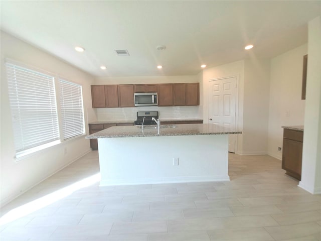 4122 Mossy Bank Ln, Houston, TX 77068 - kitchen featuring stainless steel microwave, stove, tasteful backsplash, an island with sink, and light stone counters