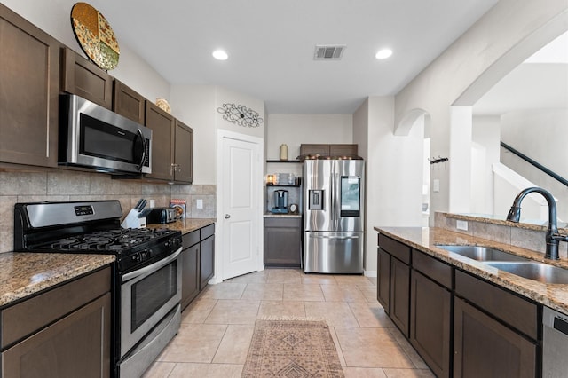 6923 Glenmoor Dr, Rosharon, TX 77583 - kitchen with stainless steel appliances, dark brown cabinets, arched walkways, light stone countertops, and decorative backsplash