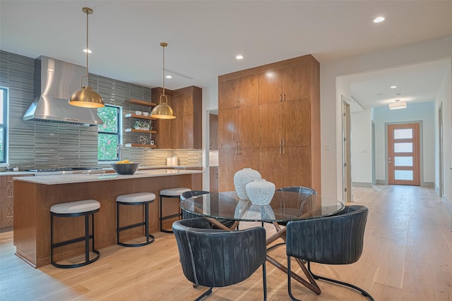 5200 Beech St, Bellaire, TX 77401 - kitchen with wall chimney exhaust hood, backsplash, light wood-style flooring, brown cabinets, and recessed lighting