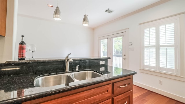 1045 W 16th St, Houston, TX 77008 - kitchen featuring brown cabinetry, light wood-style floors, dark stone countertops, and hanging light fixtures
