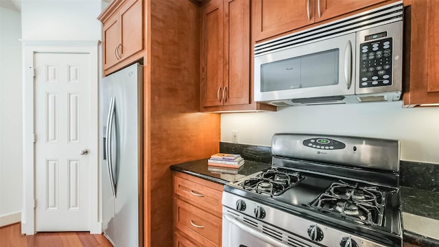 1045 W 16th St, Houston, TX 77008 - kitchen featuring appliances with stainless steel finishes, brown cabinets, light wood-style floors, and dark stone counters