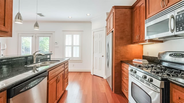 1045 W 16th St, Houston, TX 77008 - kitchen featuring appliances with stainless steel finishes, brown cabinetry, light wood-style flooring, dark stone counters, and pendant lighting