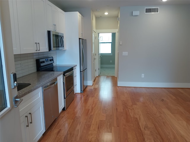 2401 Crawford St Unit A109, Houston, TX 77004 - kitchen with stainless steel appliances, light wood-style floors, white cabinets, stone countertops, and decorative backsplash