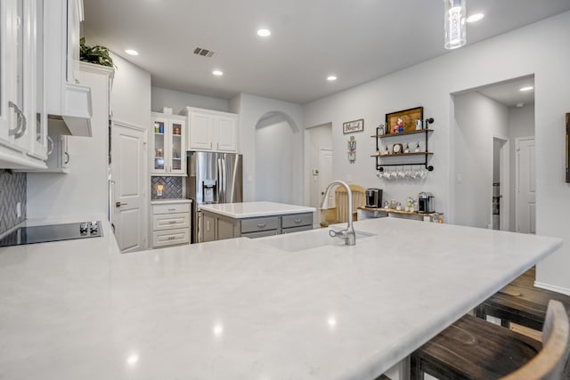 23007 Birchwood Valley Ln, Katy, TX 77493 - kitchen with arched walkways, black electric cooktop, stainless steel fridge, a center island, and light countertops