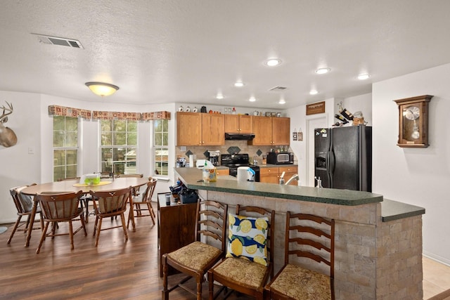 164 Sea Gull Dr, Livingston, TX 77351 - kitchen featuring black appliances, under cabinet range hood, wood finished floors, tasteful backsplash, and dark countertops