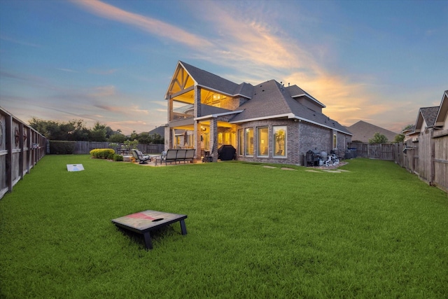 13627 Saddlebred Springs Ln, Cypress, TX 77429 - back of house at dusk featuring a fenced backyard, a balcony, brick siding, a patio area, and roof with shingles