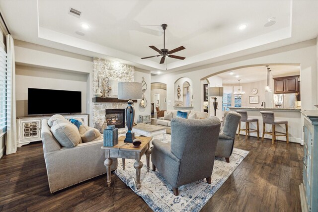 13627 Saddlebred Springs Ln, Cypress, TX 77429 - living area featuring a raised ceiling, arched walkways, a ceiling fan, a fireplace, and dark wood-style flooring
