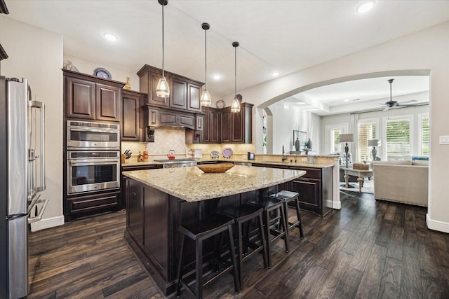 13627 Saddlebred Springs Ln, Cypress, TX 77429 - kitchen with a peninsula, arched walkways, stainless steel appliances, dark brown cabinetry, and recessed lighting