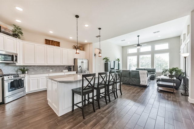 10119 Napier Dr, Iowa Colony, TX 77583 - kitchen with stainless steel appliances, dark wood-style floors, a kitchen breakfast bar, backsplash, and an island with sink