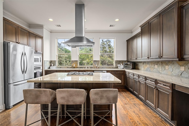 1616 Nevada St, Houston, TX 77006 - kitchen with appliances with stainless steel finishes, island exhaust hood, a kitchen breakfast bar, a kitchen island, and light wood-type flooring