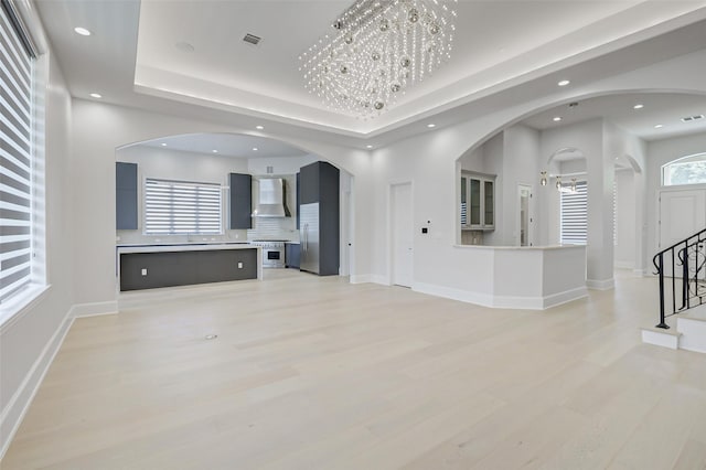 2822 Westgrove Ln, Houston, TX 77027 - unfurnished living room with light wood-style flooring, arched walkways, recessed lighting, a chandelier, and a tray ceiling