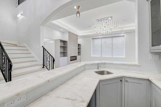 2822 Westgrove Ln, Houston, TX 77027 - kitchen featuring light stone counters, gray cabinets, a raised ceiling, arched walkways, and glass insert cabinets