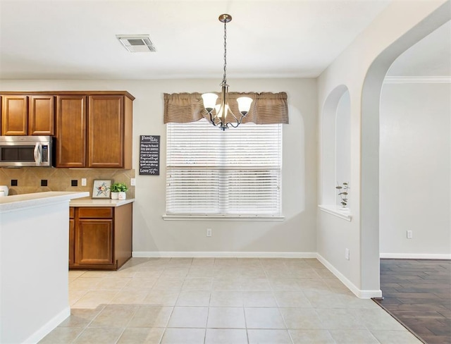 23931 Clover Trl, Katy, TX 77494 - kitchen featuring stainless steel microwave, a chandelier, brown cabinetry, light countertops, and pendant lighting