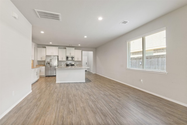 16833 Pink Wintergreen Dr, Conroe, TX 77385 - kitchen with appliances with stainless steel finishes, open floor plan, light wood finished floors, a kitchen island with sink, and white cabinetry
