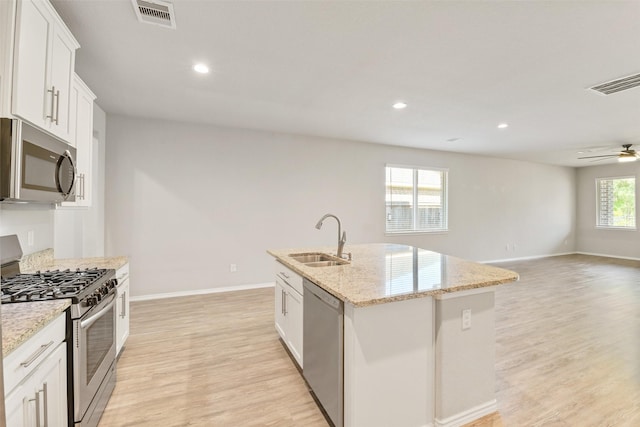 16833 Pink Wintergreen Dr, Conroe, TX 77385 - kitchen featuring appliances with stainless steel finishes, light wood-type flooring, ceiling fan, an island with sink, and light stone countertops