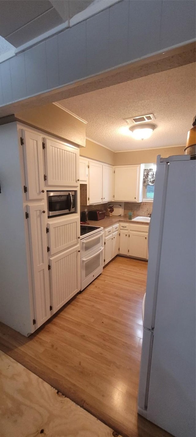 20 Connor Ln, Huntsville, TX 77320 - kitchen with white appliances, light wood-style flooring, white cabinets, light countertops, and a textured ceiling