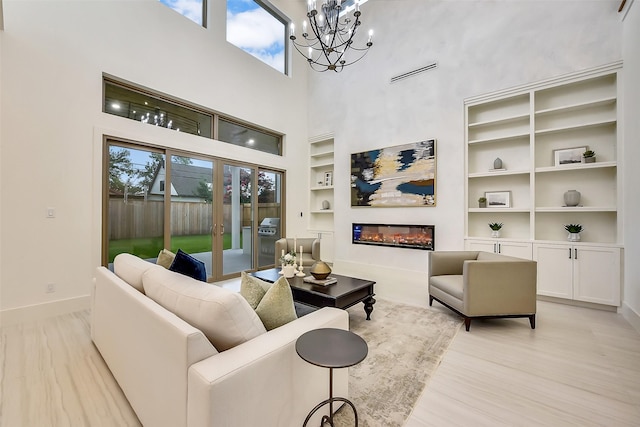 7106 Dearborn St, Houston, TX 77055 - living area featuring built in features, a chandelier, a glass covered fireplace, light wood-style flooring, and a towering ceiling