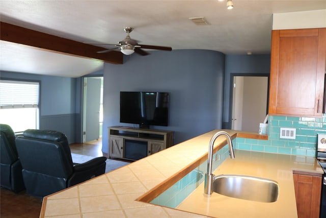 16542 John Silver Rd, Jamaica Beach, TX 77554 - kitchen with open floor plan, a ceiling fan, backsplash, brown cabinets, and a wainscoted wall