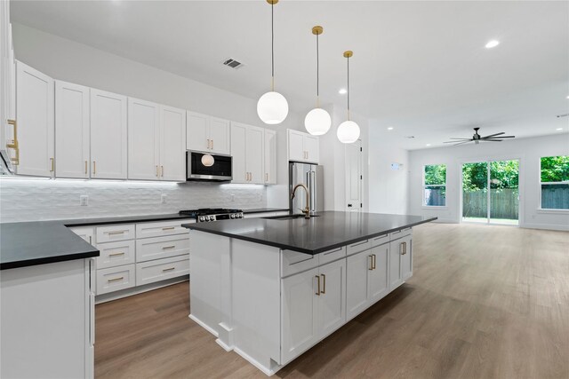 412 E 34th St, Houston, TX 77018 - kitchen featuring dark countertops, appliances with stainless steel finishes, light wood-style floors, backsplash, and white cabinetry