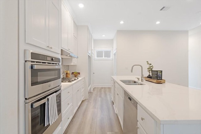 6723 Saint Augustine St, Houston, TX 77021 - kitchen with appliances with stainless steel finishes, white cabinets, under cabinet range hood, a kitchen island with sink, and light wood-type flooring