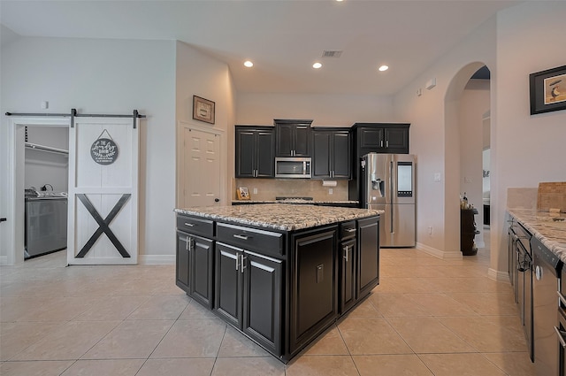 4227 Lodge Ranch Ct, Fulshear, TX 77441 - kitchen featuring dark cabinets, stainless steel appliances, washer / clothes dryer, arched walkways, and light tile patterned floors