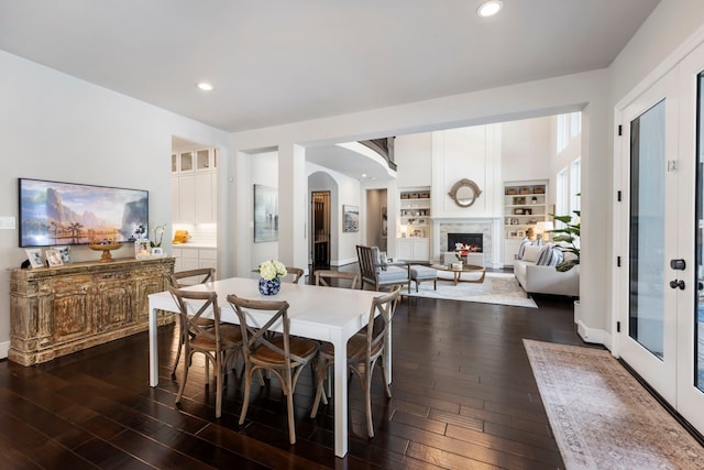 8550 Tombron Grove Rd, Magnolia, TX 77354 - dining room featuring dark wood finished floors, a warm lit fireplace, arched walkways, recessed lighting, and built in shelves
