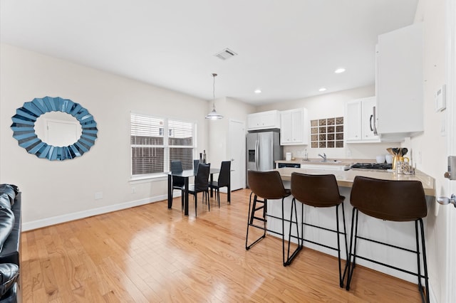 3736 Main Poplar Dr, Houston, TX 77025 - kitchen with stainless steel fridge, a peninsula, a kitchen breakfast bar, light countertops, and light wood-style floors