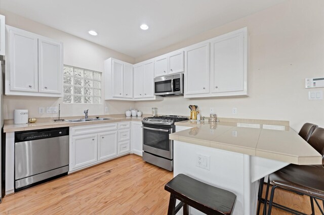 3736 Main Poplar Dr, Houston, TX 77025 - kitchen featuring stainless steel appliances, a peninsula, a kitchen breakfast bar, white cabinets, and light wood-type flooring