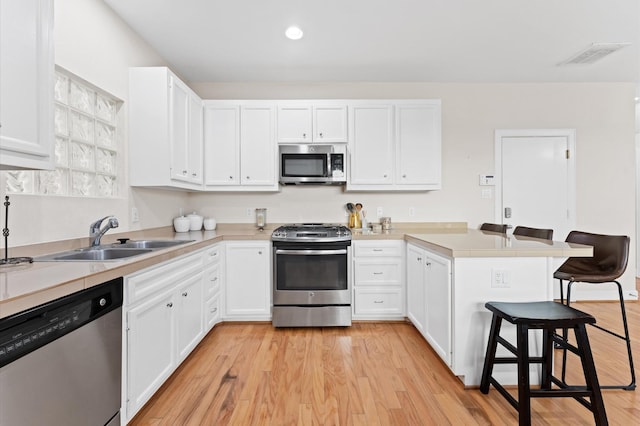 3736 Main Poplar Dr, Houston, TX 77025 - kitchen featuring appliances with stainless steel finishes, a peninsula, a kitchen bar, white cabinetry, and recessed lighting