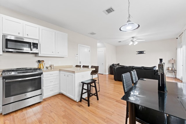 3736 Main Poplar Dr, Houston, TX 77025 - kitchen with stainless steel appliances, a peninsula, white cabinetry, and light wood-style floors