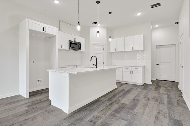 7922 Sealey St, Houston, TX 77088 - kitchen with stainless steel microwave, white cabinetry, light wood finished floors, tasteful backsplash, and recessed lighting