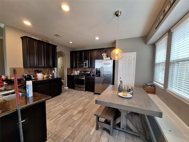 20331 Weeping Pine Way, Richmond, TX 77407 - kitchen featuring stainless steel appliances, arched walkways, backsplash, light wood finished floors, and hanging light fixtures