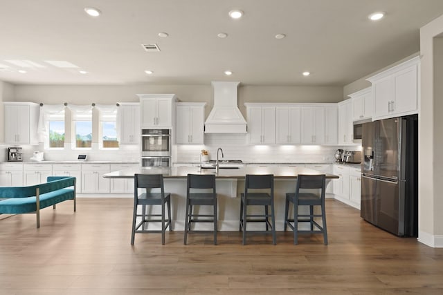 6919 Shoreline View Dr, Katy, TX 77493 - kitchen featuring appliances with stainless steel finishes, custom exhaust hood, decorative backsplash, a kitchen breakfast bar, and white cabinetry