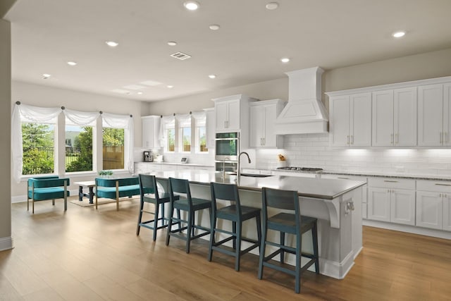 6919 Shoreline View Dr, Katy, TX 77493 - kitchen featuring custom exhaust hood, an island with sink, tasteful backsplash, white cabinetry, and recessed lighting