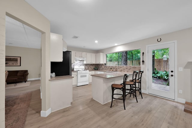 58 Sandpebble Dr, Spring, TX 77381 - kitchen featuring white range with gas stovetop, freestanding refrigerator, a peninsula, white cabinetry, and decorative backsplash