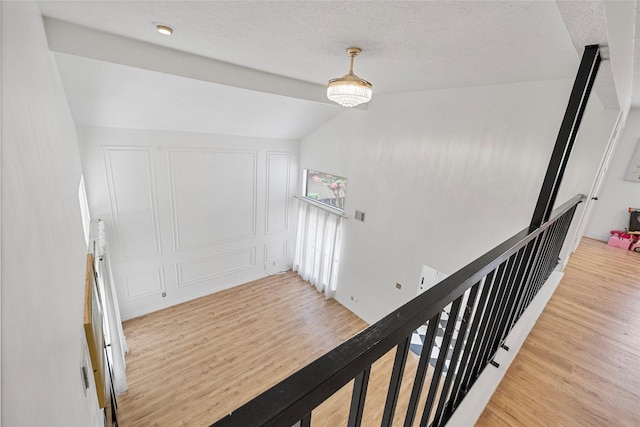 8033 Oakwood Forest Dr, Houston, TX 77040 - hallway with light wood-style flooring, an upstairs landing, a decorative wall, lofted ceiling, and a textured ceiling