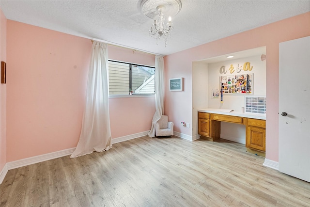 8033 Oakwood Forest Dr, Houston, TX 77040 - unfurnished bedroom with light wood finished floors, a chandelier, built in desk, and a textured ceiling