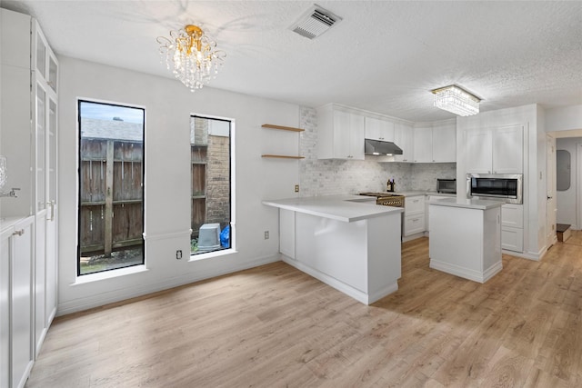 8033 Oakwood Forest Dr, Houston, TX 77040 - kitchen featuring stainless steel microwave, a chandelier, under cabinet range hood, white cabinets, and a textured ceiling