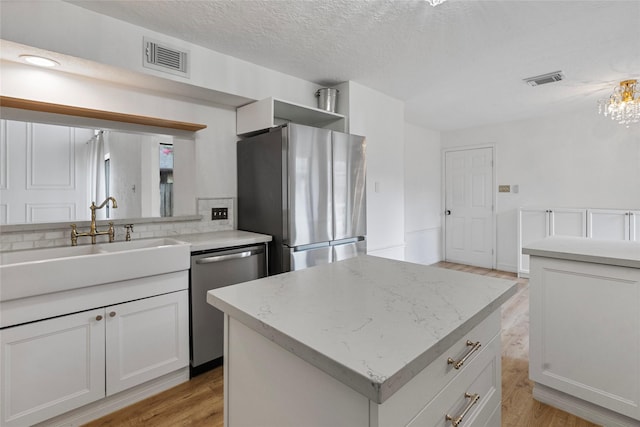 8033 Oakwood Forest Dr, Houston, TX 77040 - kitchen featuring stainless steel appliances, light wood finished floors, a kitchen island, white cabinetry, and a chandelier