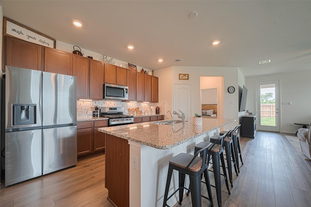 7227 Birchville Dr, Rosharon, TX 77583 - kitchen with appliances with stainless steel finishes, light wood-type flooring, decorative backsplash, light stone counters, and a kitchen bar