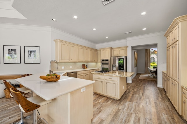 13722 Vinery Ln, Cypress, TX 77429 - kitchen with stainless steel appliances, cream cabinetry, a breakfast bar area, a peninsula, and light wood-style flooring