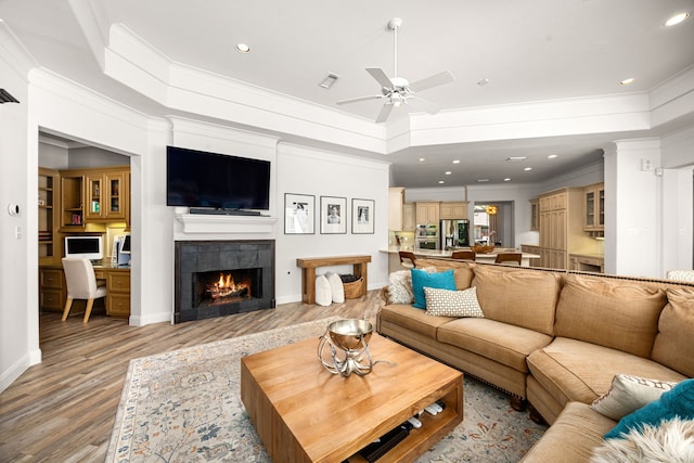 13722 Vinery Ln, Cypress, TX 77429 - living room featuring light wood-style flooring, ornamental molding, ceiling fan, a tile fireplace, and a raised ceiling