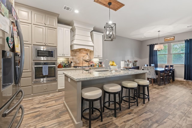 2619 Portland Ave, College Station, TX 77845 - kitchen featuring stainless steel appliances, custom exhaust hood, light wood finished floors, backsplash, and a breakfast bar area