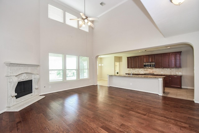 5506 Plumero Meadow Dr, Katy, TX 77494 - unfurnished living room featuring arched walkways, a ceiling fan, a premium fireplace, a towering ceiling, and wood finished floors