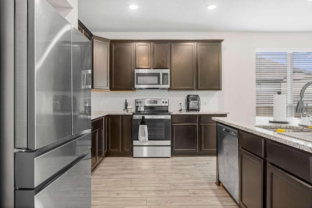 1925 Viva Rd, Bryan, TX 77807 - kitchen featuring stainless steel appliances, dark brown cabinets, light wood-style floors, backsplash, and light stone countertops