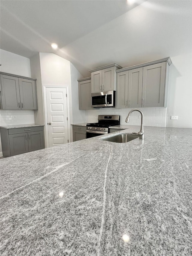 4301 Fenwick Rd, Texas City, TX 77591 - kitchen with appliances with stainless steel finishes, gray cabinetry, decorative backsplash, lofted ceiling, and light stone counters