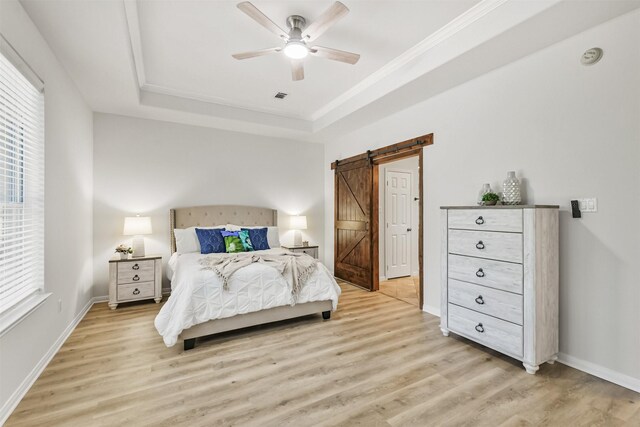 8006 Sports Haven Dr, Humble, TX 77346 - bedroom with a barn door, light wood-style flooring, a tray ceiling, crown molding, and a ceiling fan