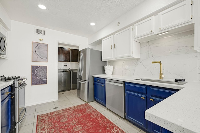 8727 Vinkins Rd, Houston, TX 77071 - kitchen with stainless steel appliances, blue cabinetry, washer and dryer, white cabinetry, and tasteful backsplash